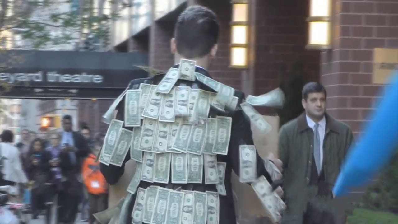 كيفية تصرف المارة إتجاه رجل يرتدي بدلة مغطاة بعشرات الدولارات