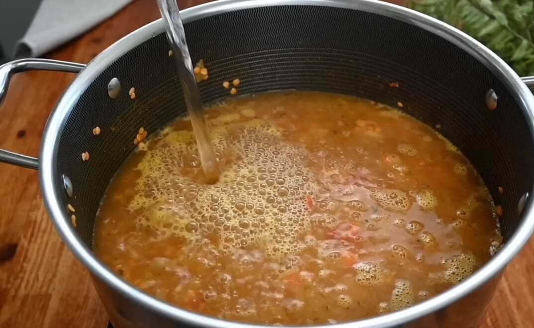 بعد ذلك نضيف الماء الساخن بحيث يغطي جميع المكونات ونقلب جيداً، ونترك الحساء على نار متوسطة لمدة 40 دقيقة أو حتى ينضج العدس.
